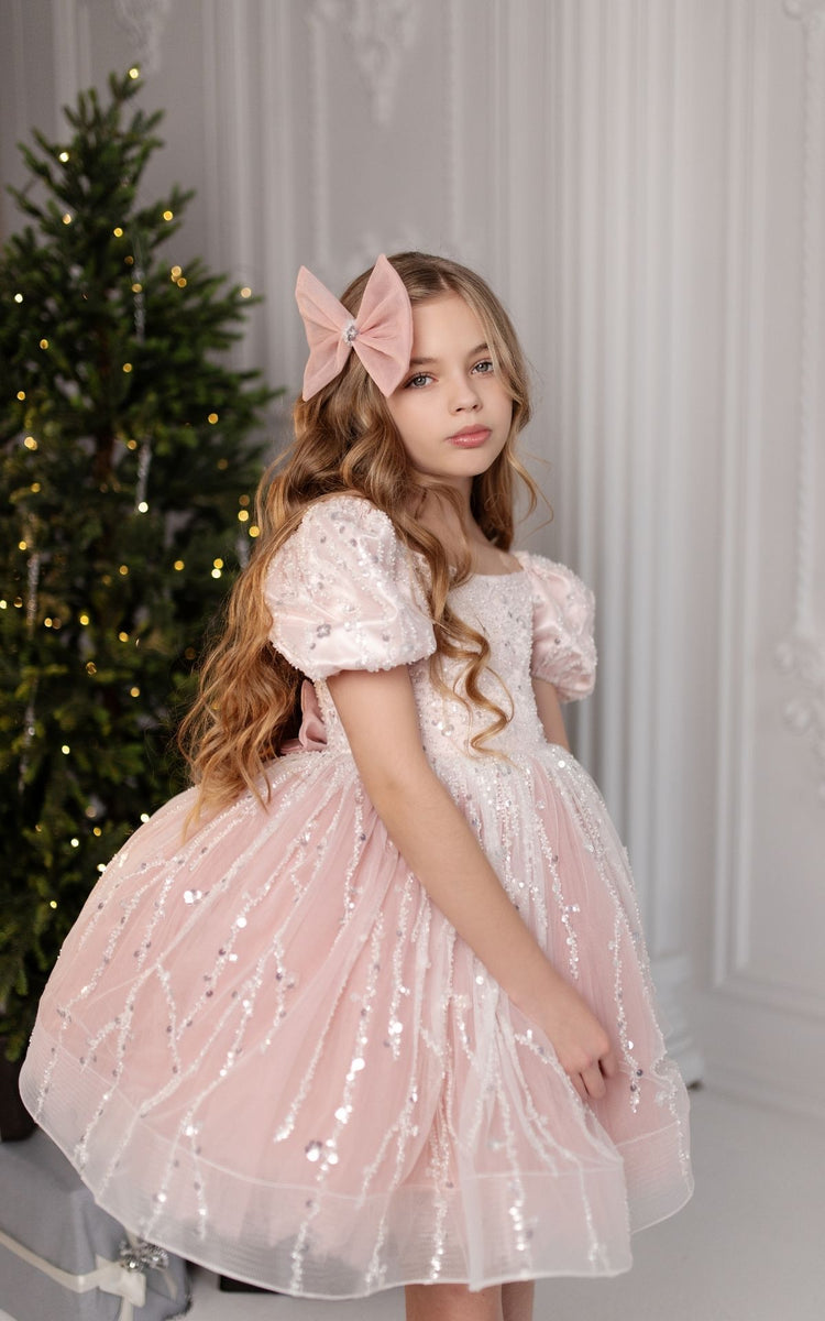 a little girl in a pink dress standing next to a christmas tree