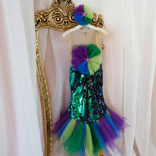 a little girl's green and purple dress hanging on a wall