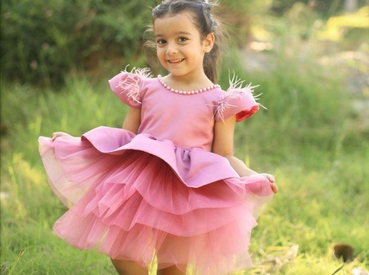 a little girl in a pink dress walking through the grass