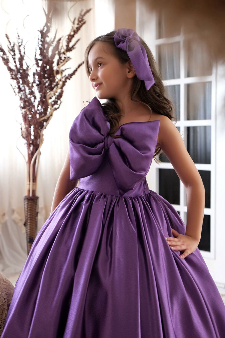 a little girl wearing a purple dress with a big bow