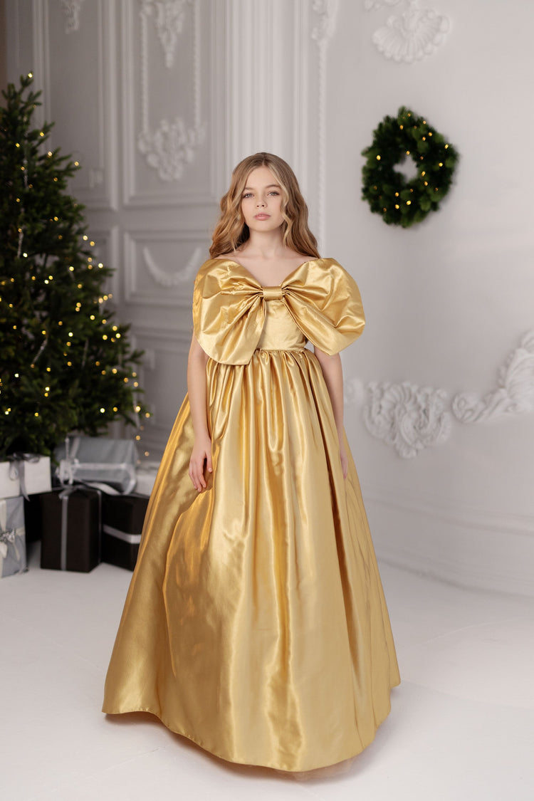 a woman in a gold dress standing in front of a christmas tree