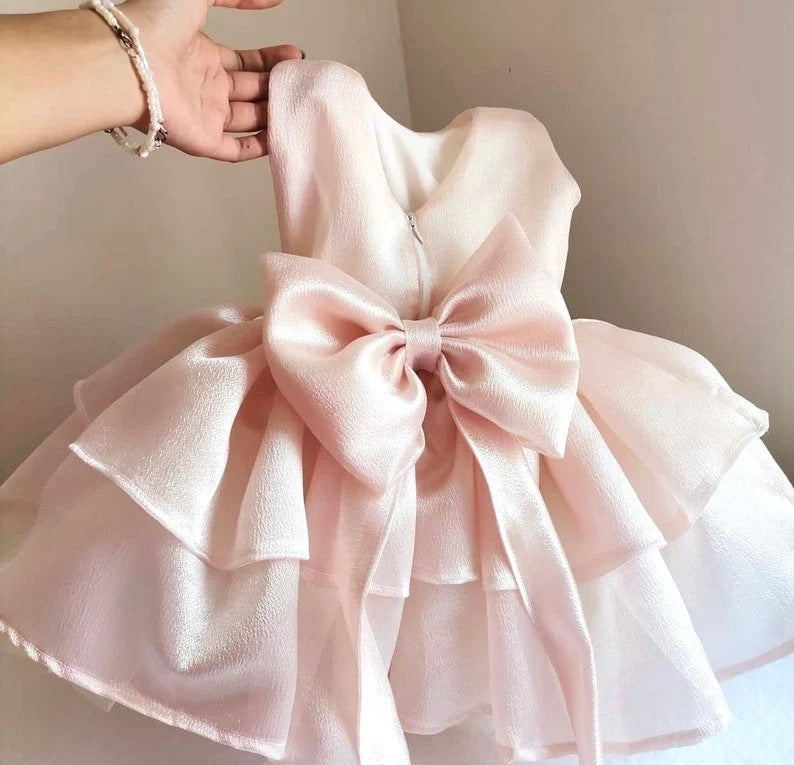 a hand holding a pink dress with a big bow