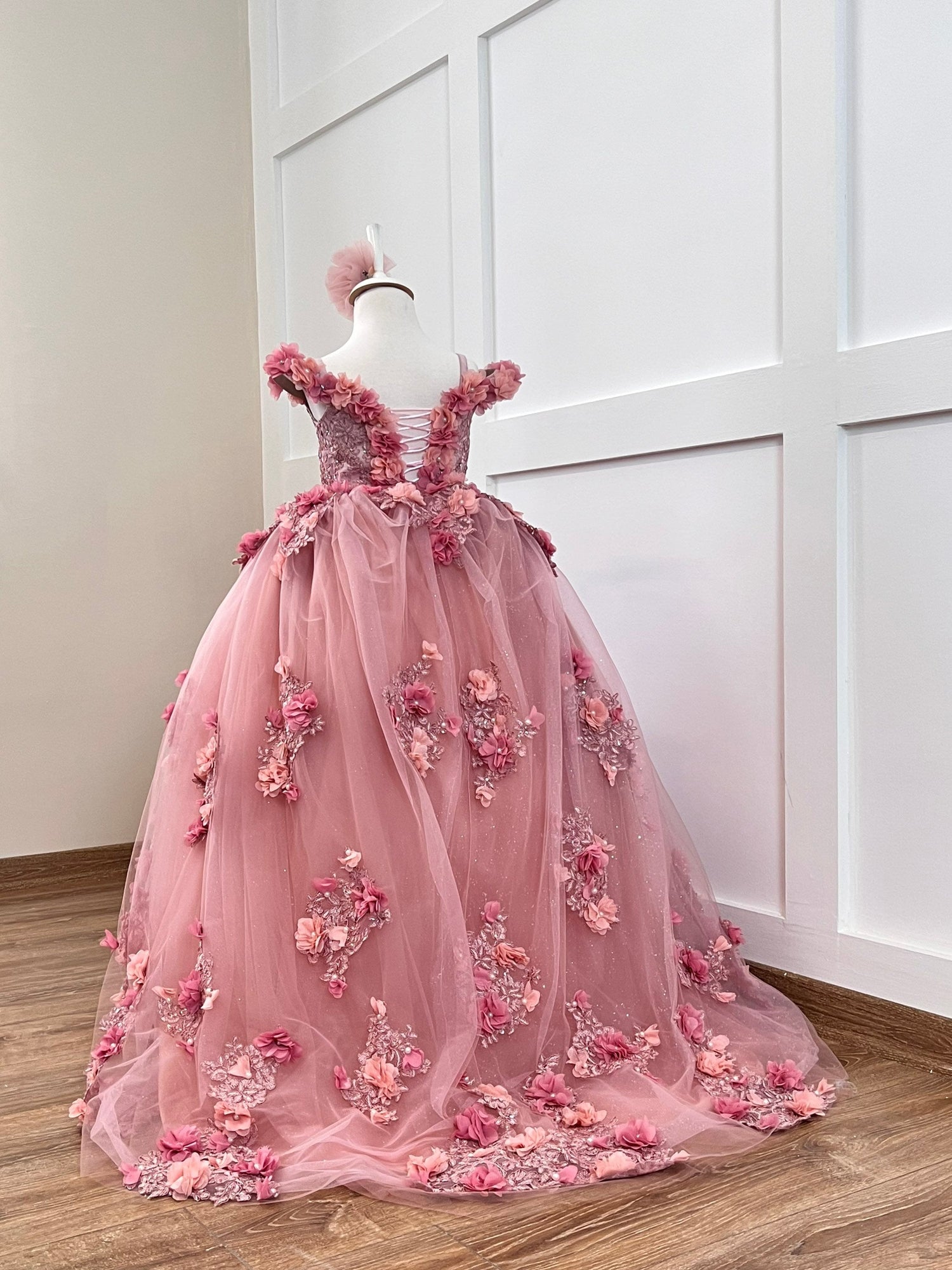 Quinceanera blush gown with satin bodice, lace, 3D colorful flowers, layered tulle skirt, and matching hair accessory.