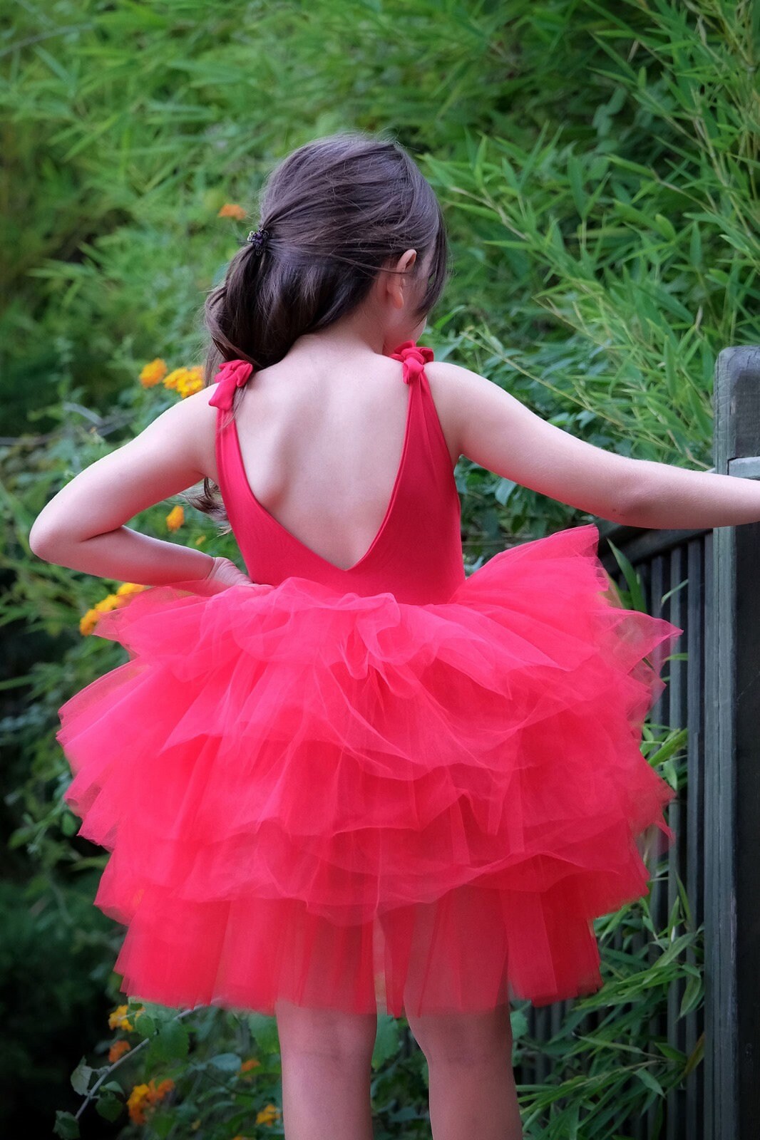 a little girl in a red dress looking over a fence