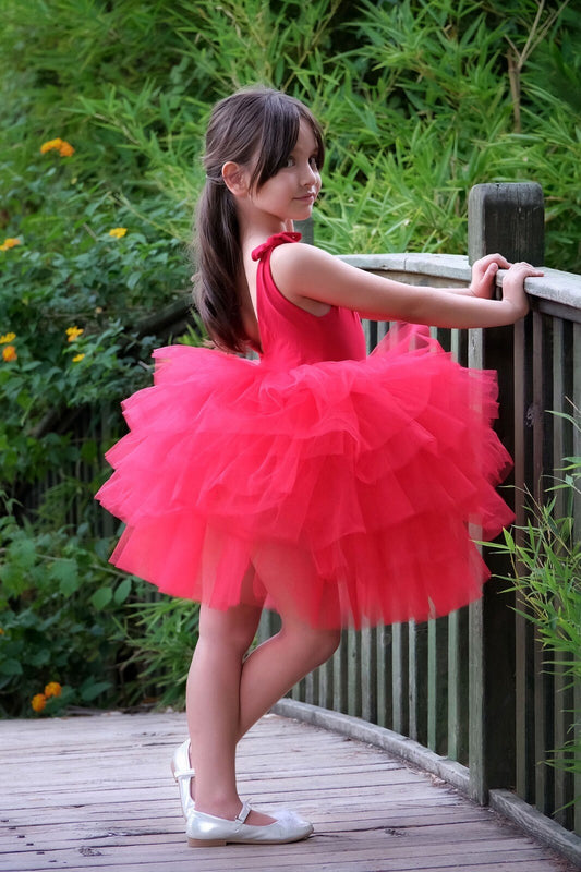 a little girl in a red dress leaning against a rail